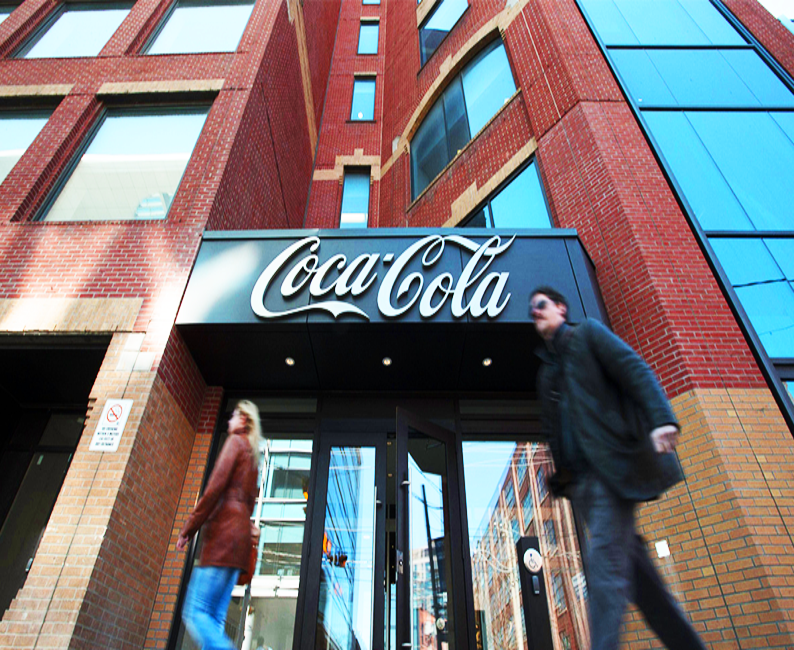 People walking in front of a large red-brick building with Coca-Cola facade