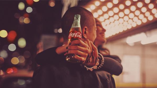 A couple hugging while a woman holds a bottle of Coca-Cola