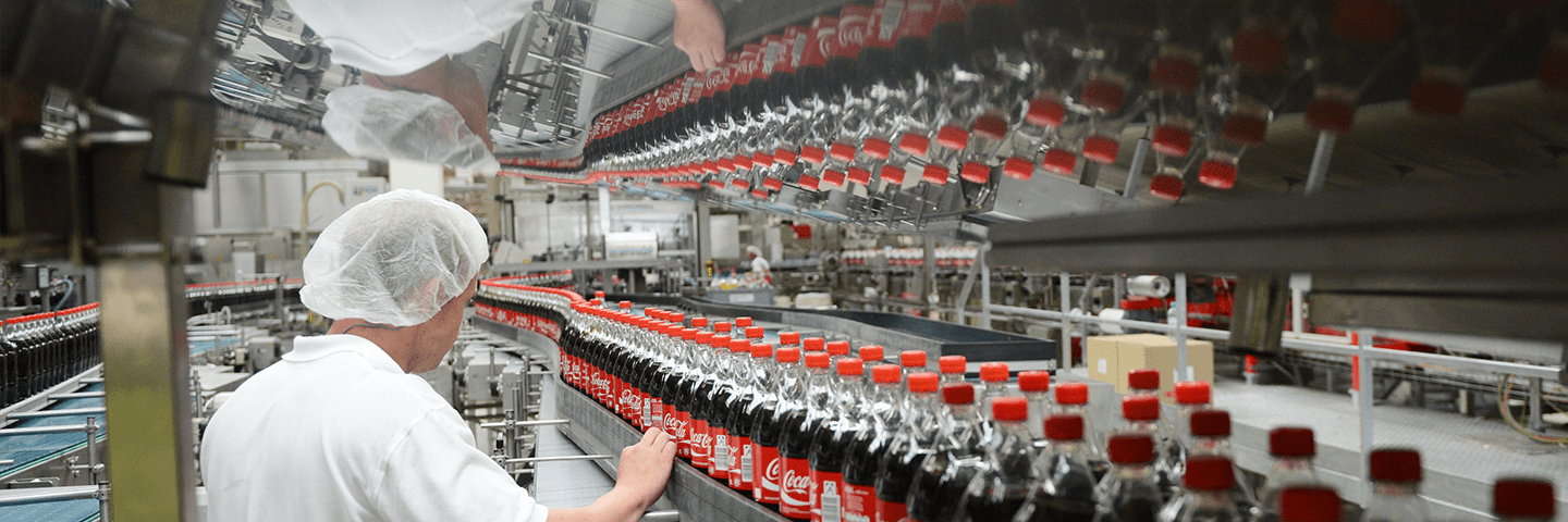 A man standing in front of an assembly line with Coca-Cola bottles