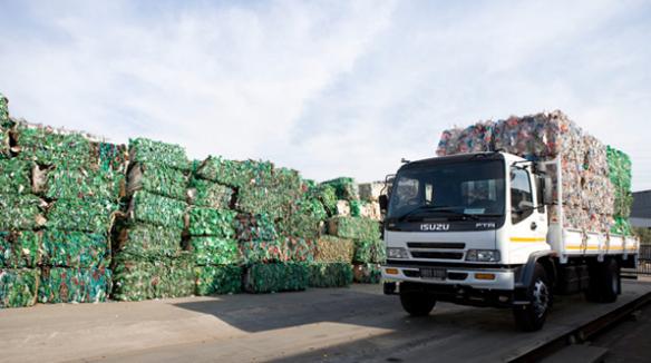 Truck loaded with large cubes of compressed plastic at a recycling facility, many more stacks of these cubes are seen in the background