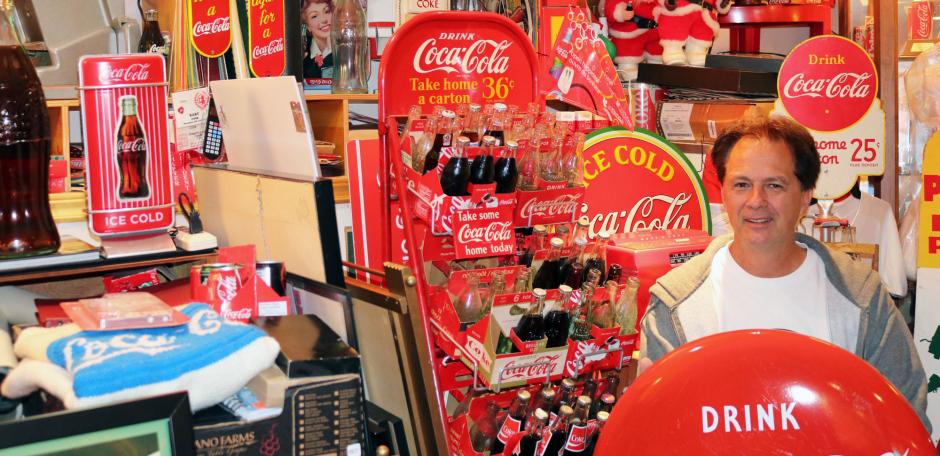 Collector Bill Cook shown standing in a room full of Coca-Cola memorabilia 
