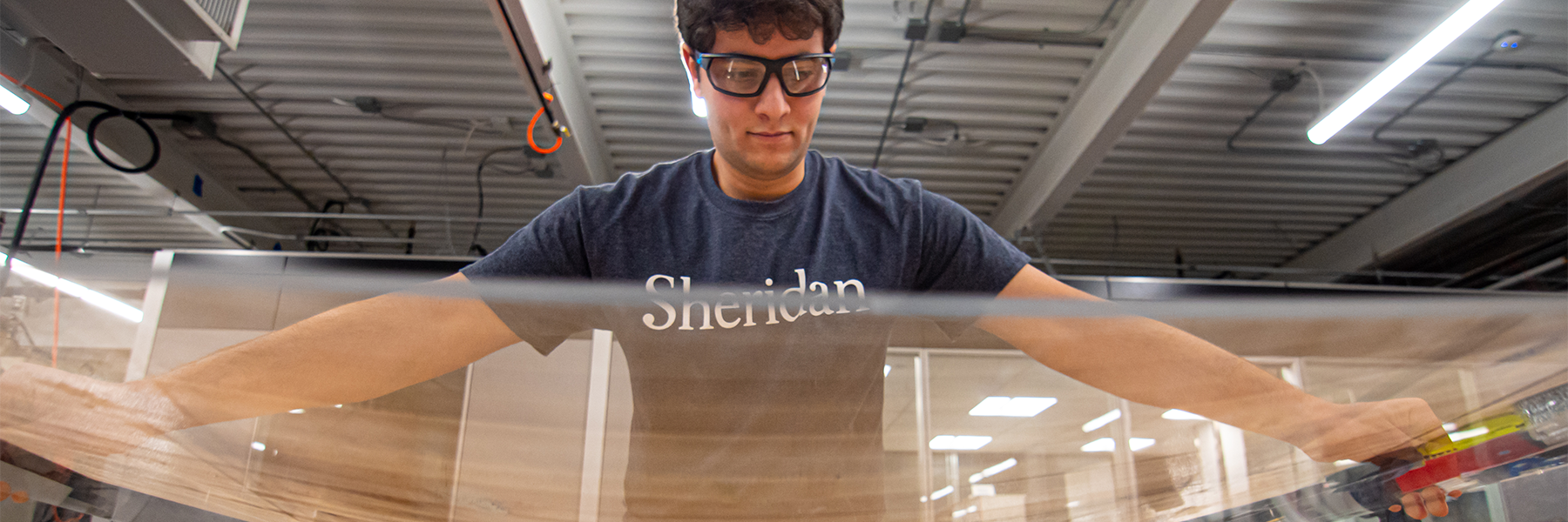 A man in a workshop holding a piece of plexiglass